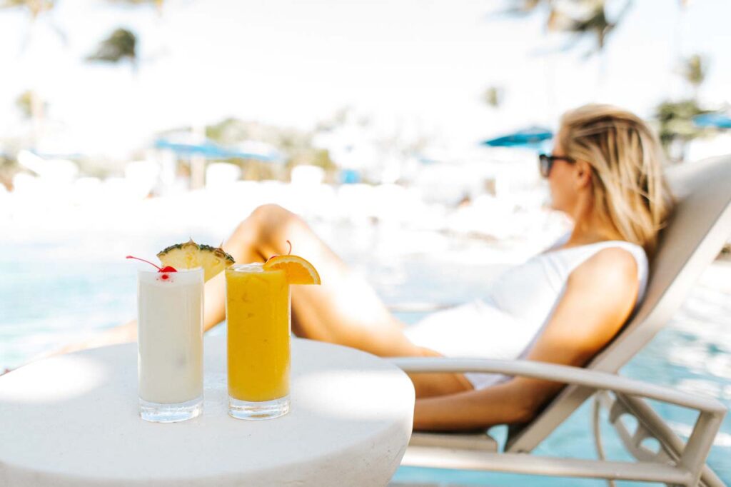 Mixed cocktails on a table beside a woman relaxing by the pool at the Capri Inn