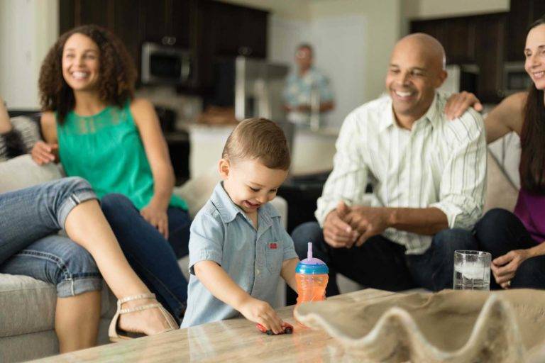 Little boy playing with a race car in front of friends and family in their Encore Resort living room
