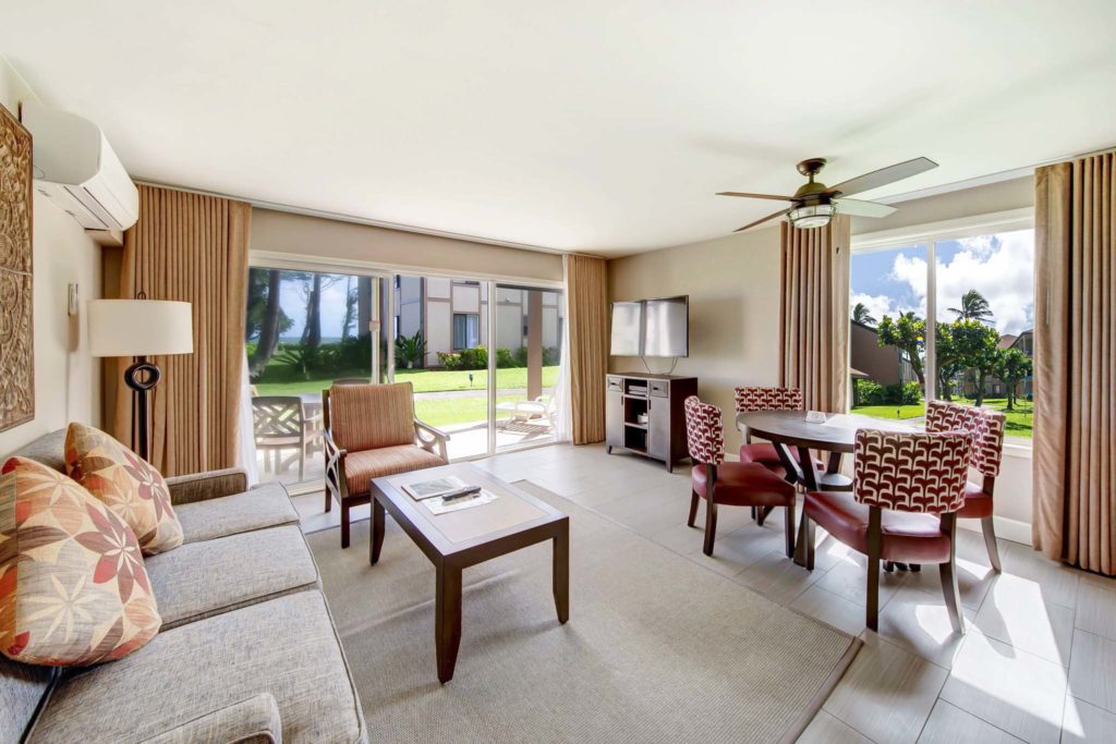 Furnished living room of a Pono Kai Resort residence with sofa, dining table, coffee table, and sliding glass doors.